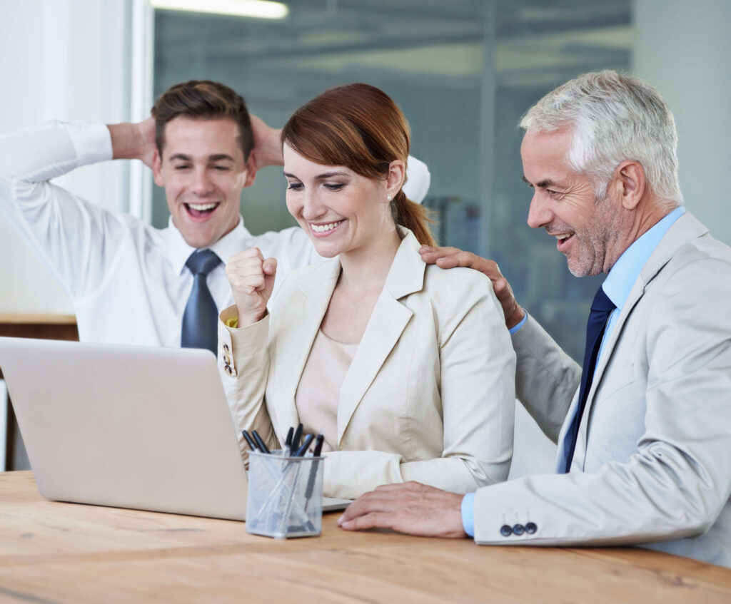 Three people in business attire celebrate in front of a laptop displaying innovative AI solutions, with one person smiling, another cheering with fists clenched, and the third resting hands on their head.