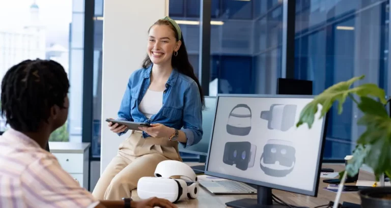 AI Person in a small business talking about the ai adoption gap, with related images on a computer monitor and VR equipment on the desk.