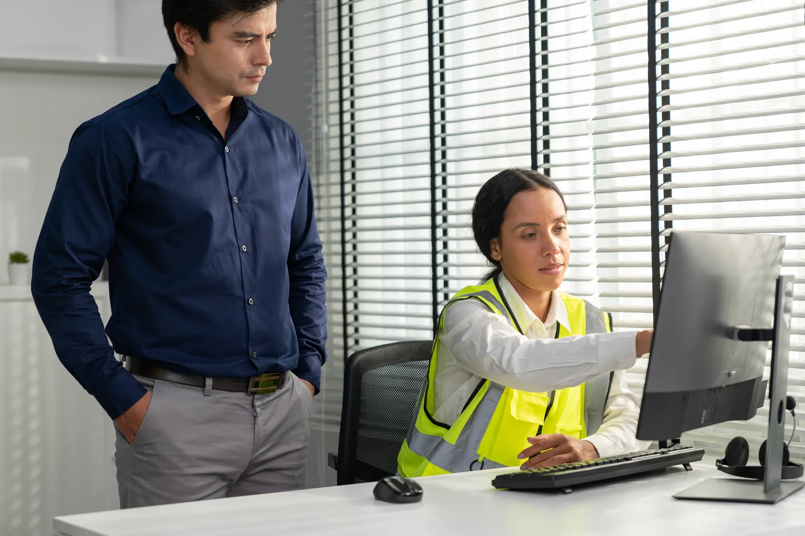 Office manager in a safety vest pointing at a scheduling screen while a business owner looks on